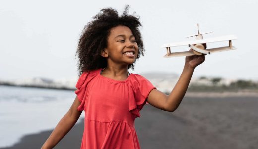 african-kid-running-on-the-beach-while-playing-with-wood-toy-airplane-focus-on-face.jpg
