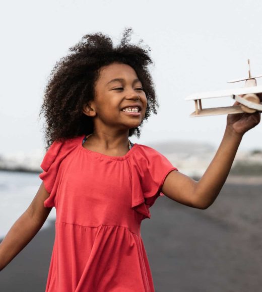 african-kid-running-on-the-beach-while-playing-with-wood-toy-airplane-focus-on-face.jpg